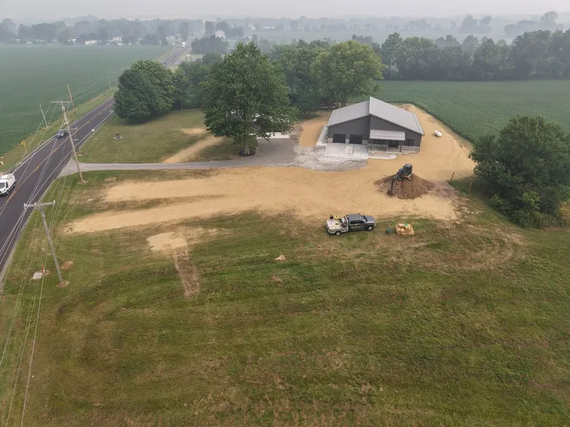 Aerial view of graded and seeded acreage around a new building beside a rural road