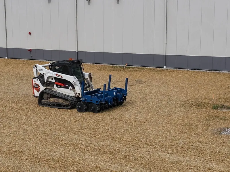 Compact track loader finish-grading beside a large commercial building