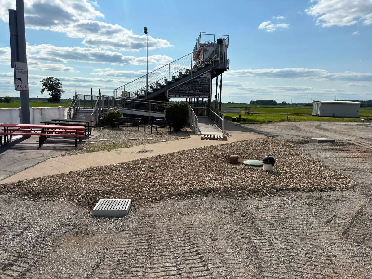 New drainage stone and graded area beside stadium bleachers at a school athletic complex
