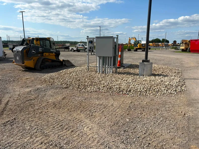 Compact track loader beside a new stone utility pad with electrical cabinets