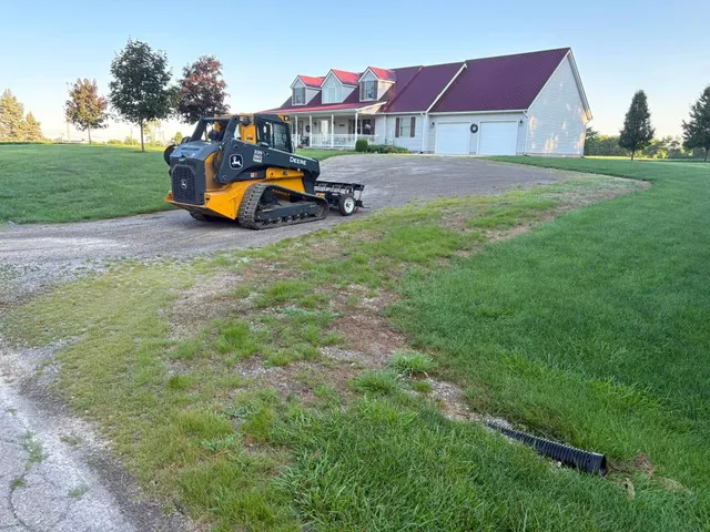 Compact track loader regrading a long gravel drive in front of a large farmhouse