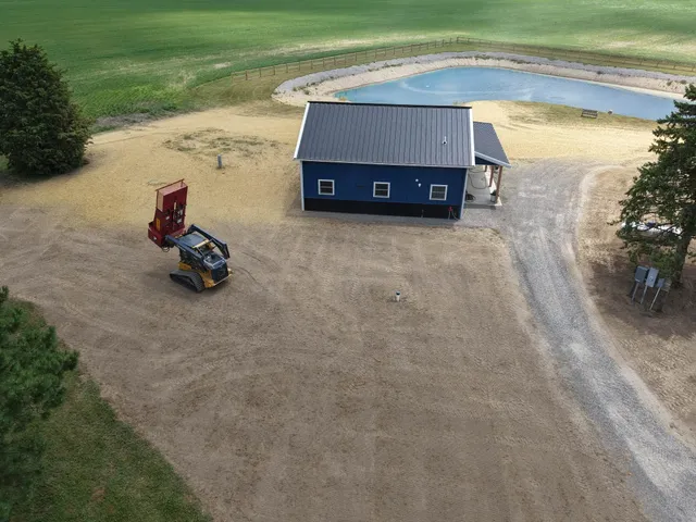 Aerial view of a newly built pond beside a pole barn on graded, seeded ground