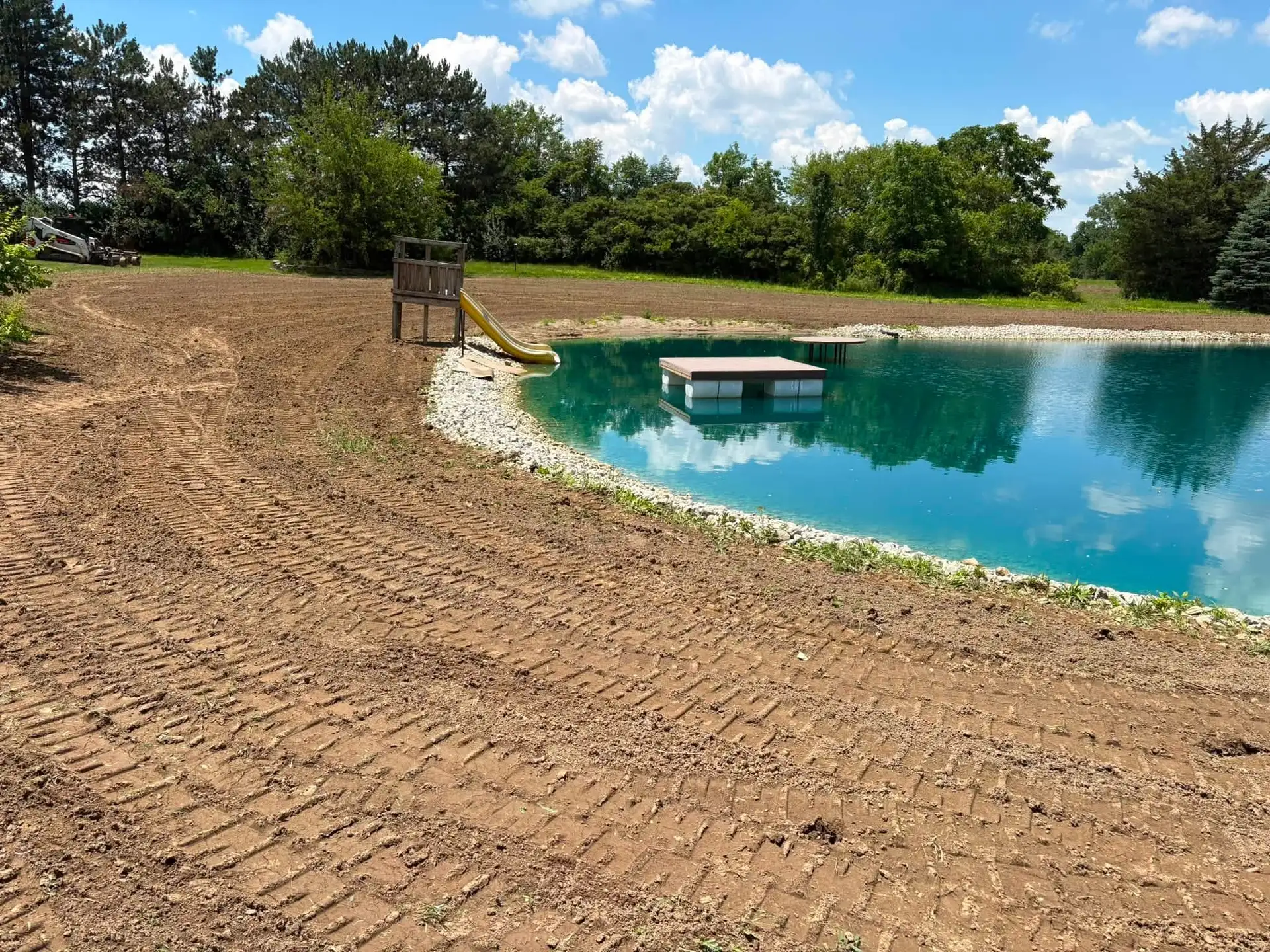 Freshly graded banks around a clear blue pond with a dock