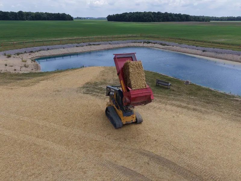 Track loader with a straw blower mulching the pond banks, seen from above